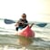 A woman wearing sunglasses and a life vest is all smiles as she paddles a sea kayak in the ocean